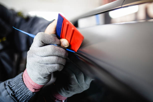 Car wrapping specialist putting vinyl foil or film on car. Selective focus.